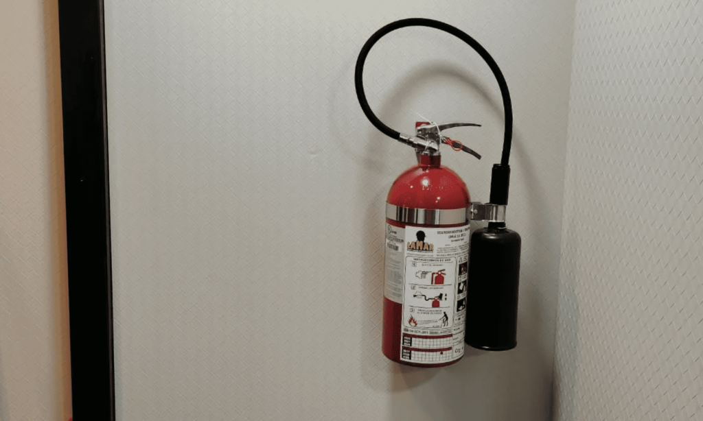 Extintor de CO2 recargado con etiqueta de servicio LAMAR y sello de seguridad, colgado en la pared con su manguera y corneta de descarga