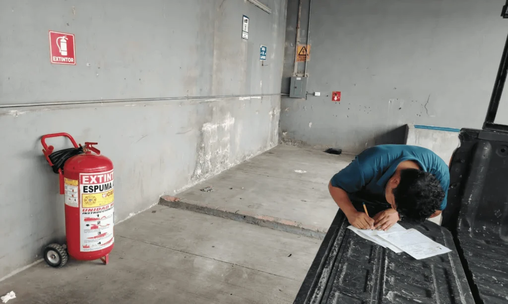 Técnico de LAMAR llenando el registro de servicio junto a un extintor de espuma sobre ruedas en un estacionamiento industrial