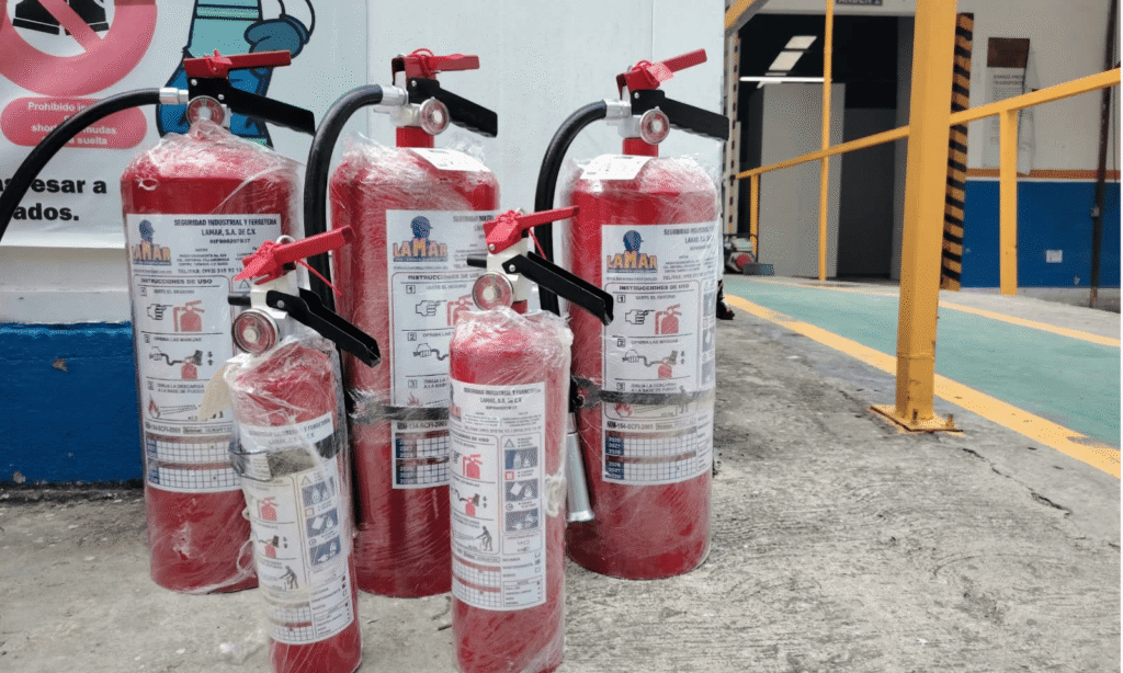 Extintores nuevos de distintas capacidades con etiqueta LAMAR, envueltos en plástico y listos para entrega en una planta industrial